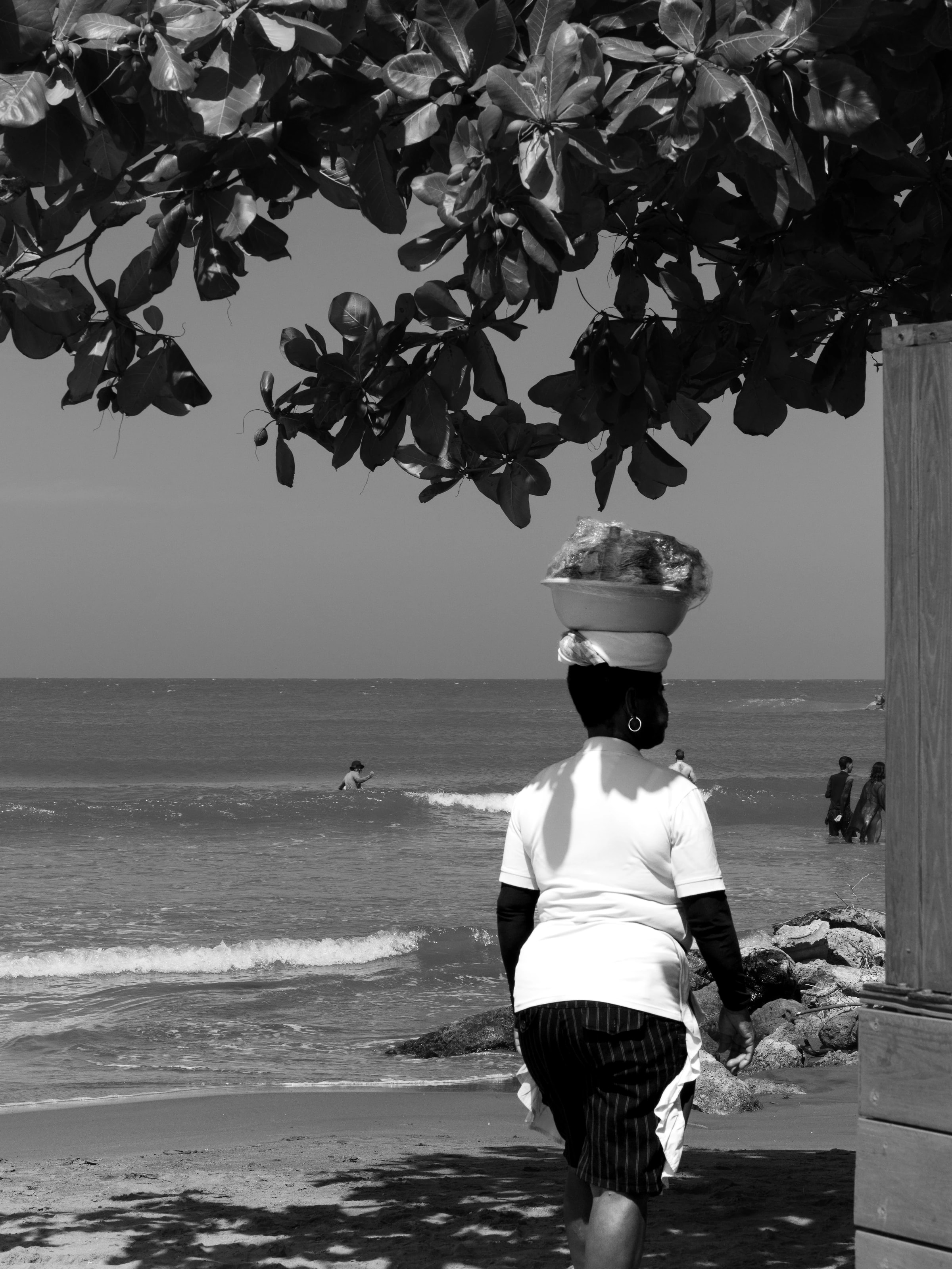 A person carrying a basket beside the sea in black and white